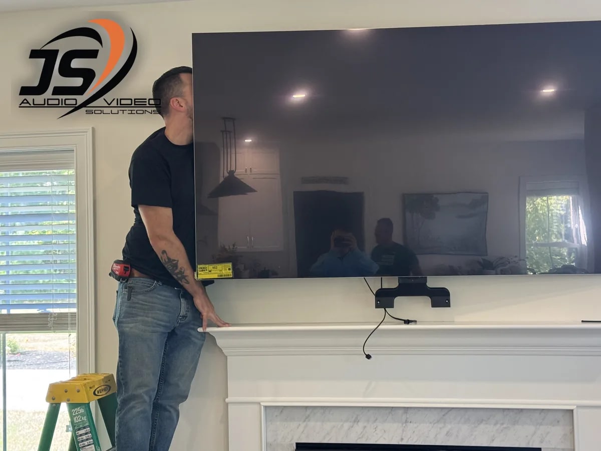 J&S Audio Video Solutions installer positioning a large television above a fireplace in Jefferson, MA
